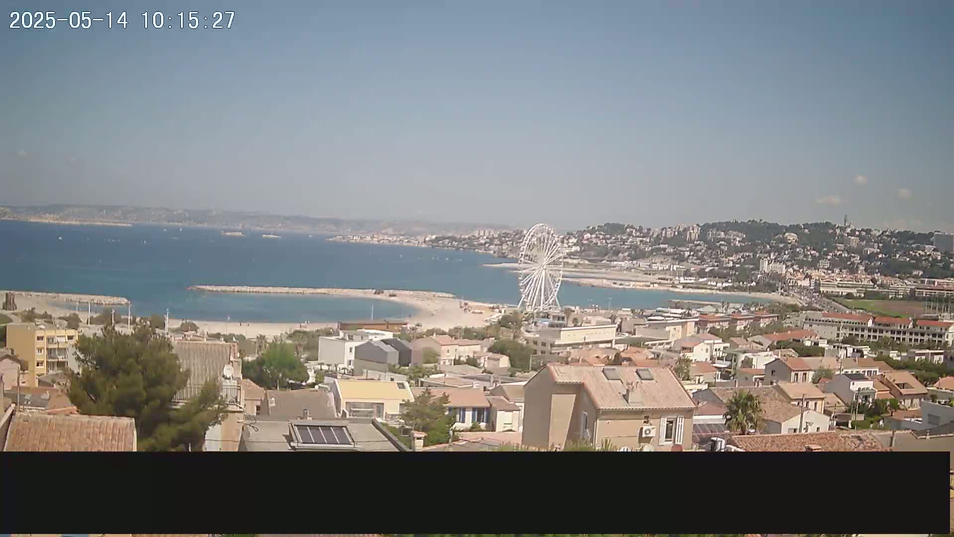 A coastal town on a sunny day with a Ferris wheel visible across a bay.