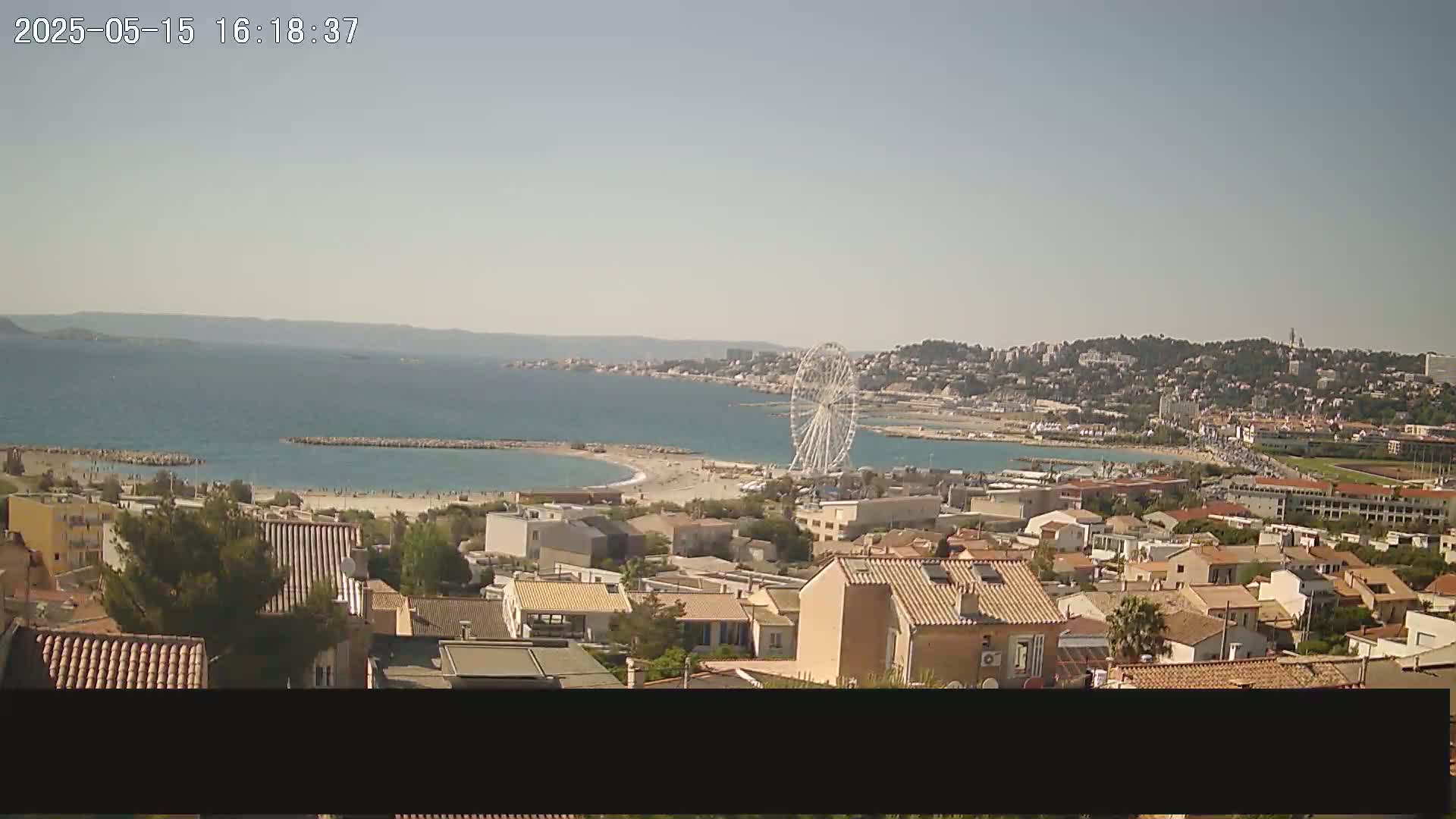 A coastal town with a Ferris wheel is visible on a sunny day, overlooking a beach and calm ocean.