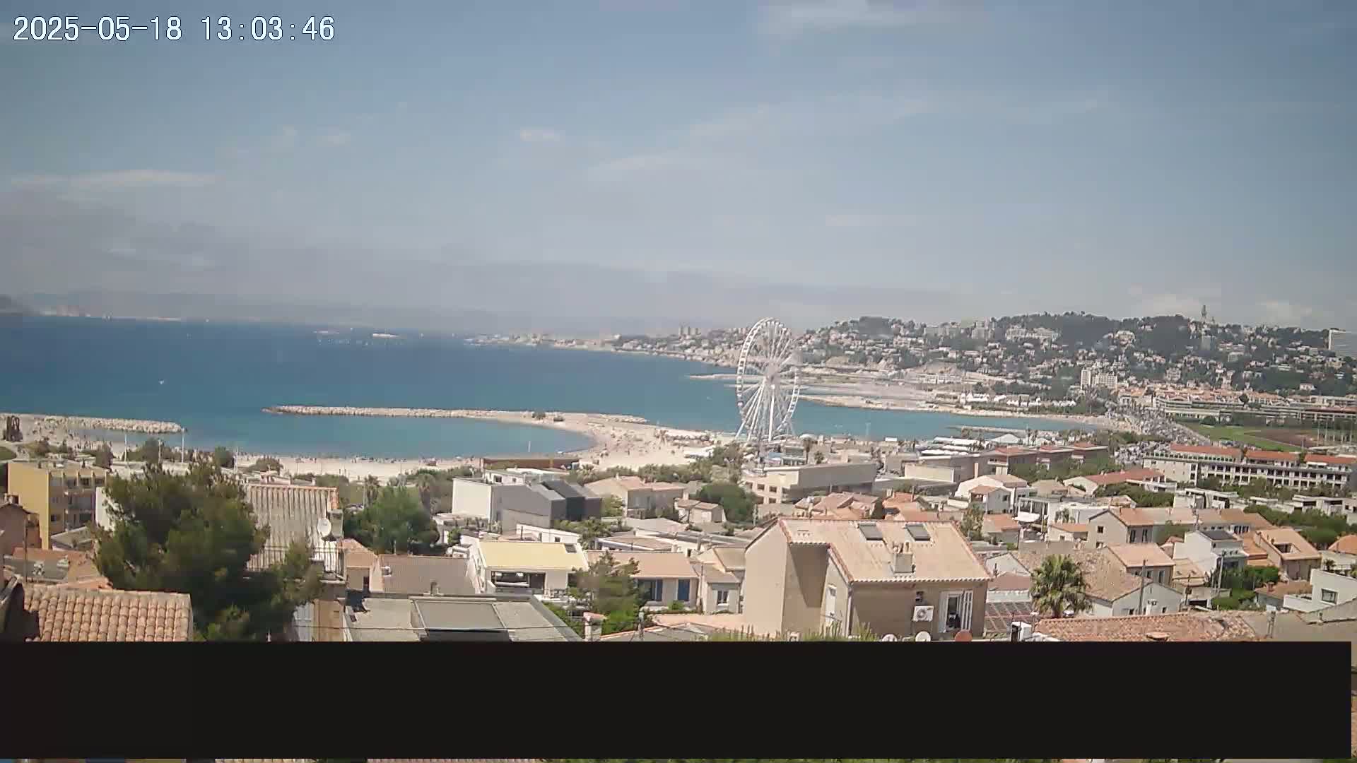 A coastal town with a Ferris wheel is visible on a sunny day, overlooking a sandy beach and calm blue ocean.