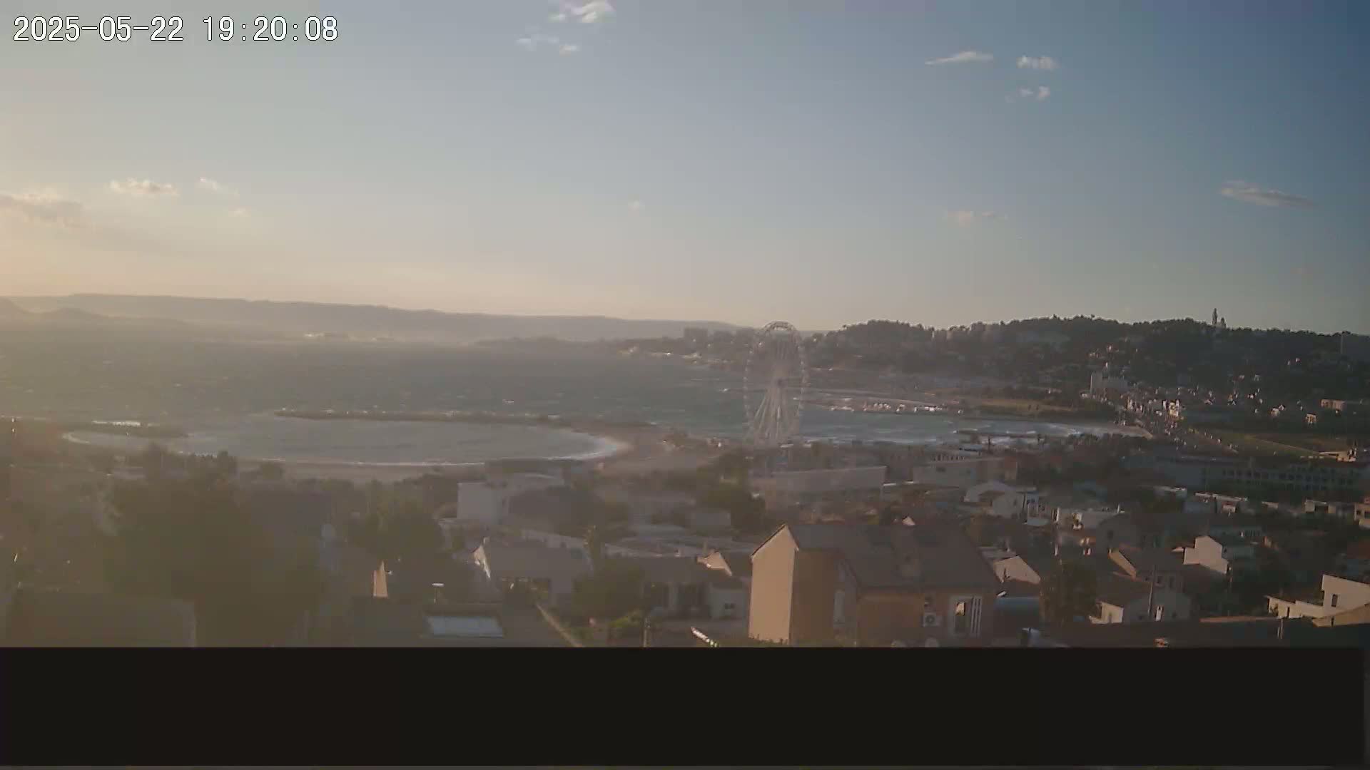A long shot of a coastal town at sunset, with a Ferris wheel visible near the beach, and somewhat choppy water.