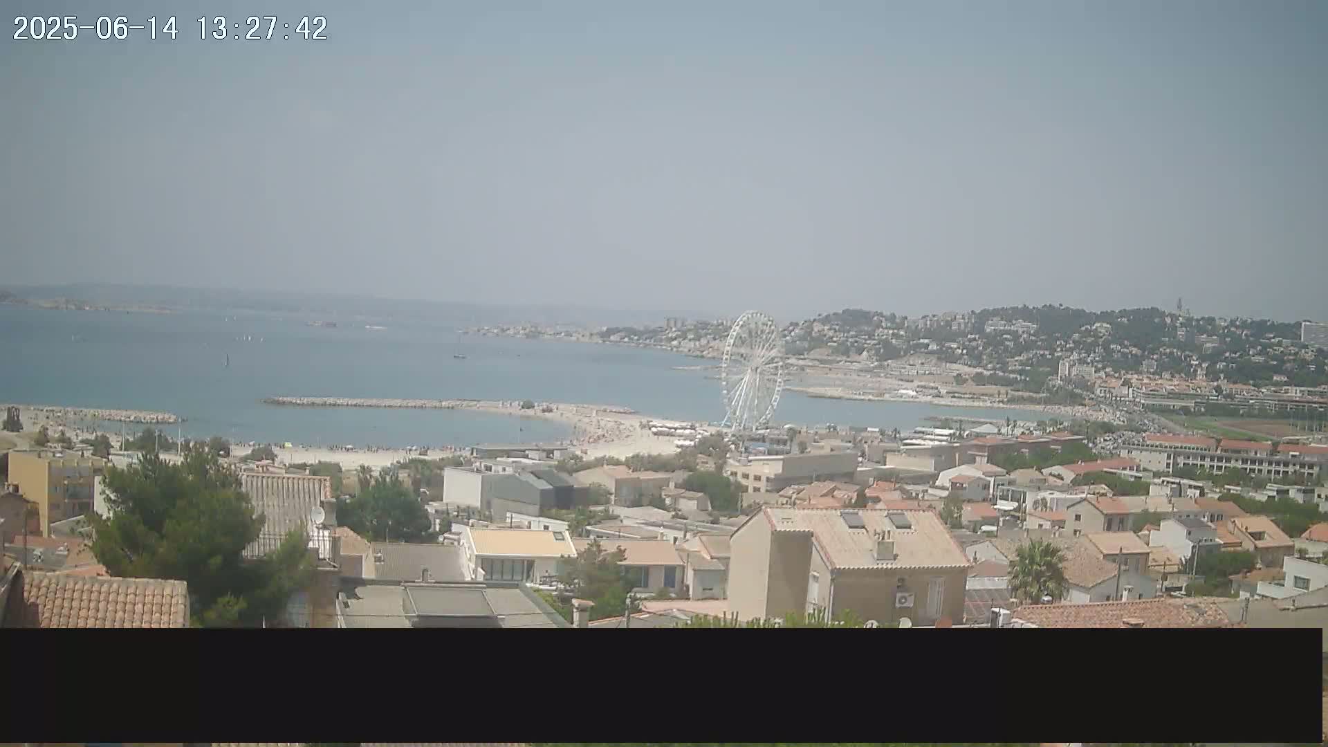 A coastal town with a Ferris wheel on a sunny day overlooks a beach with calm water.