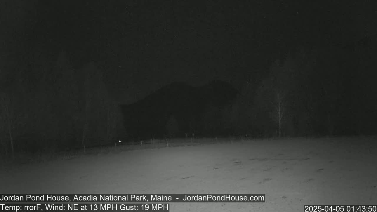 A nighttime, snow-covered field is visible with a dark hill and sparsely wooded area in the background under a dark sky with a northeast wind at 13 mph and gusts up to 19 mph.