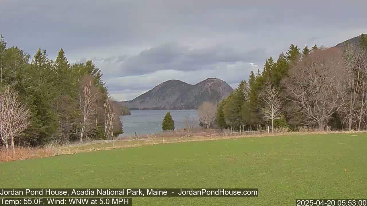 A calm body of water is nestled between tree-lined shores, with a pair of mountains in the background under a cloudy sky.