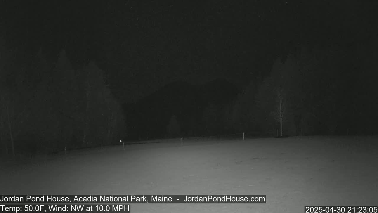 A nighttime, snow-covered field is bordered by dark trees under a dark sky with a northwest wind at 10 mph and a temperature of 50°F.