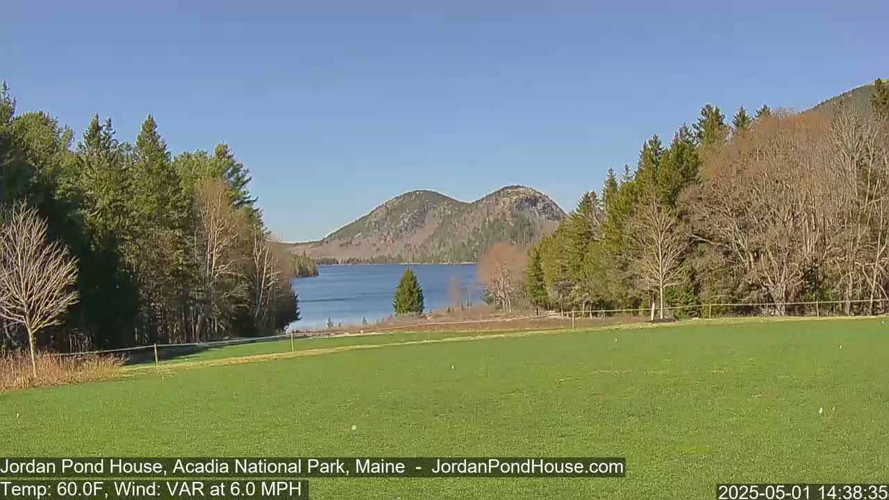 A calm, sunny day reveals a verdant field overlooking a tranquil lake nestled between tree-covered hills.
