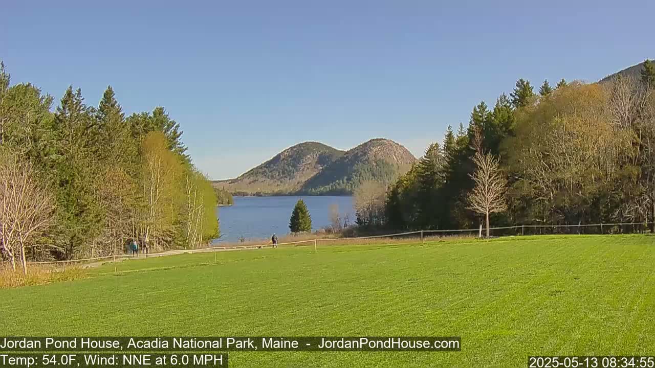 A calm, sunny day reveals a verdant field overlooking a tranquil lake nestled between verdant hills.