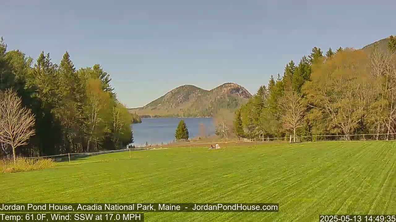A calm, sunny day reveals a verdant field overlooking a lake nestled between wooded hills.