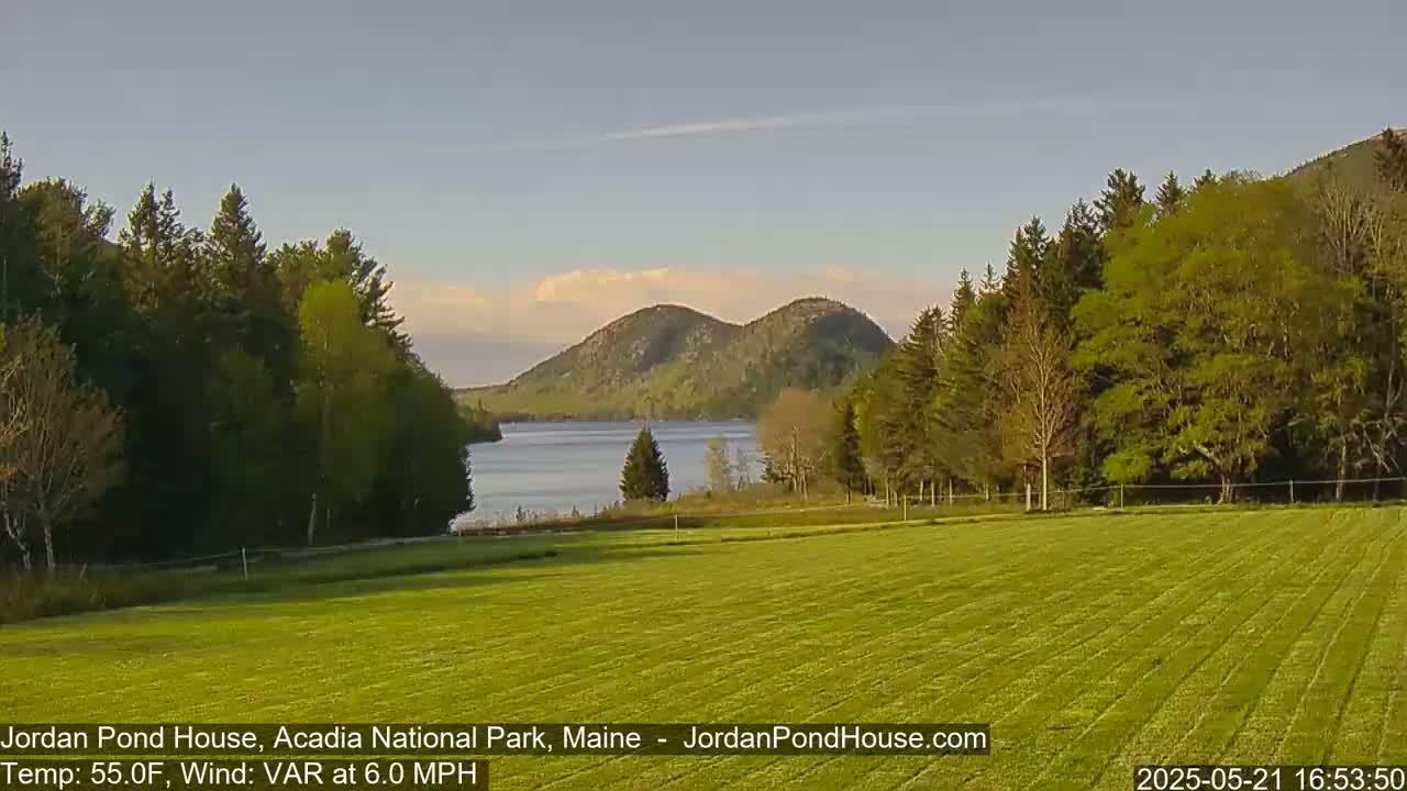 A tranquil lake nestled between verdant hills and forests under a partly cloudy, calm sky.