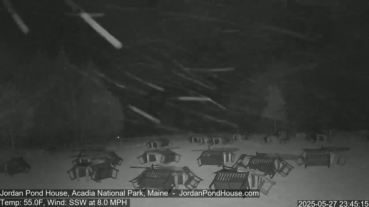 A snowy nighttime scene shows numerous overturned patio chairs scattered across a snow-covered ground in a strong wind.