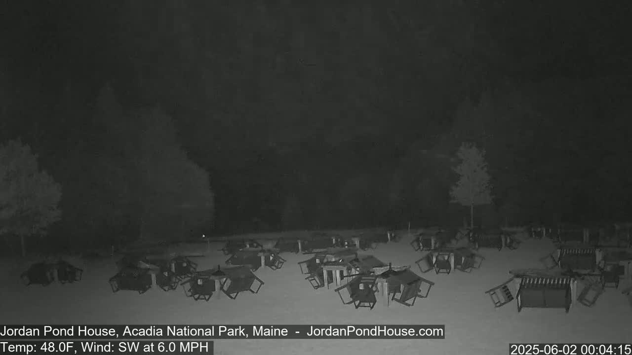 A nighttime, snowy scene shows numerous overturned picnic tables and chairs scattered across a field under a dark sky with a southwest wind.