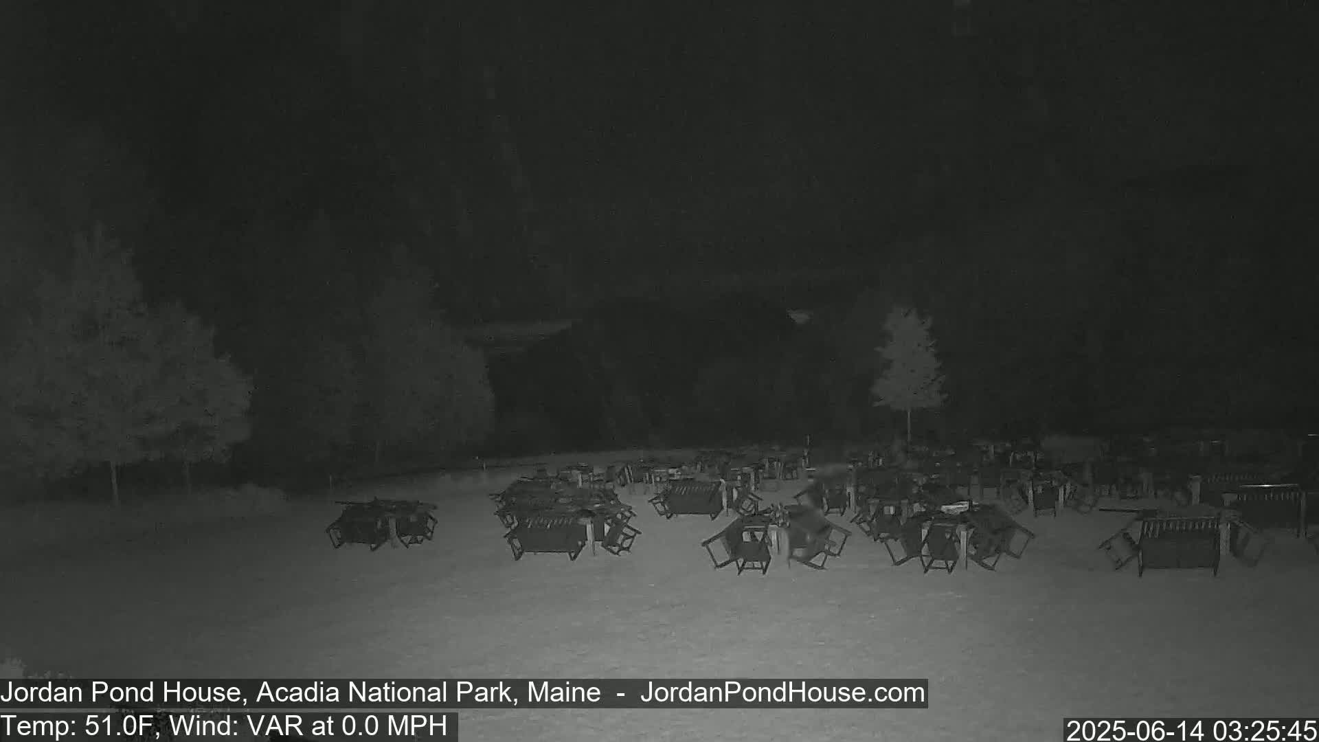 Under a dark night sky, numerous overturned tables and chairs are scattered across a mostly empty outdoor area.