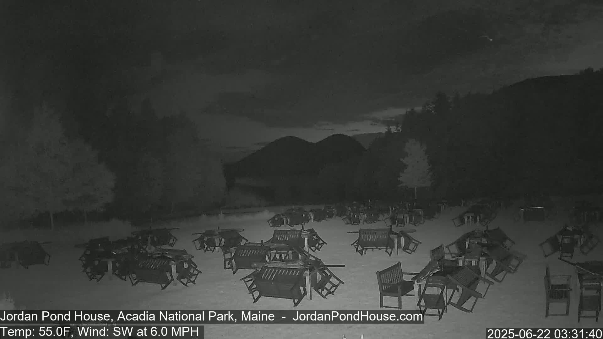 Numerous overturned tables and chairs are scattered across a grassy area at night under a dark sky with a southwest wind.