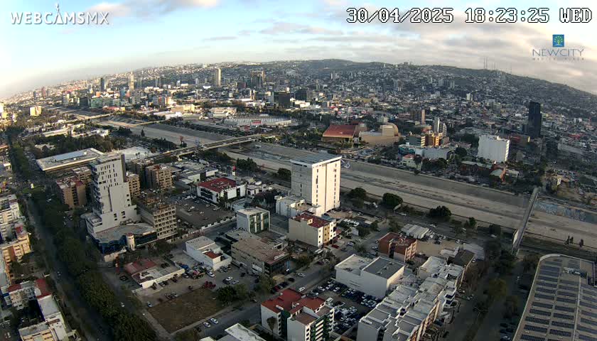 An aerial view of a sprawling city under partly cloudy skies, showing a wide highway cutting through the urban landscape.