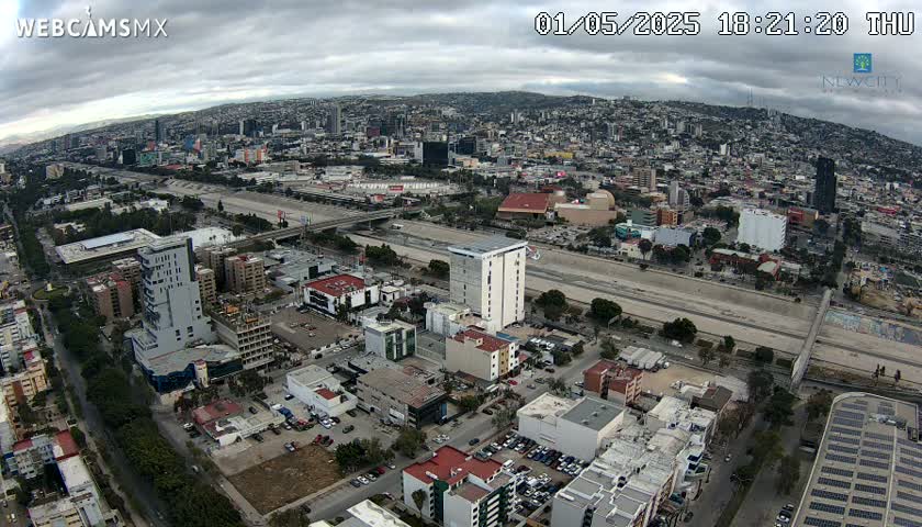 An aerial view of a city on an overcast day shows a large highway cutting through the urban landscape.