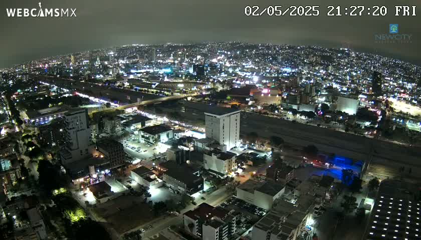An aerial nighttime view of a city with brightly lit buildings and roadways under a clear sky.