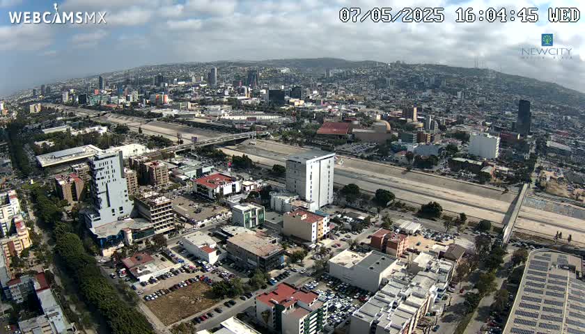An aerial view of a city on a partly cloudy day shows a large highway cutting through the urban landscape.