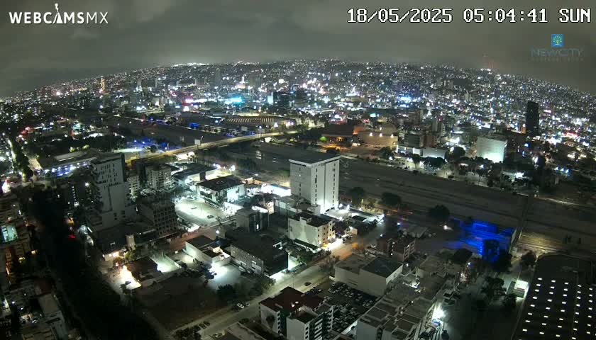 A nighttime aerial view of a city illuminated by streetlights under a cloudy sky.