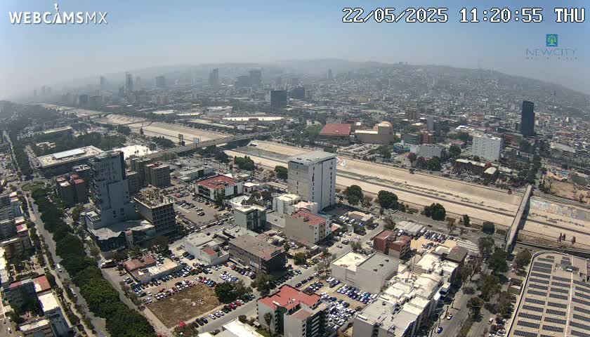 An aerial view of a city on a hazy day shows a wide river or canal running through a densely populated urban area with many buildings and parking lots.