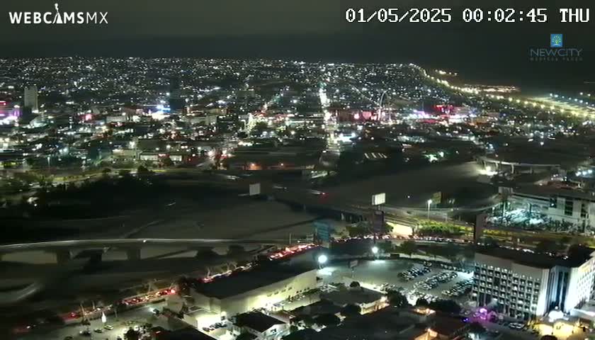 A nighttime, high-angle view of a sprawling city illuminated by numerous lights, showing roadways and buildings.