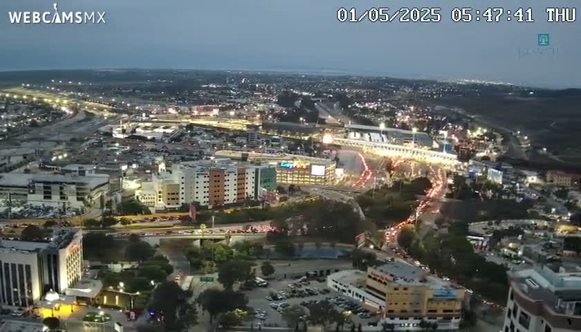 An aerial nighttime view shows a city with numerous buildings and busy roadways, under a twilight sky.