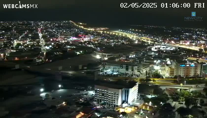 A nighttime aerial view shows a brightly lit city sprawling across a dark landscape.