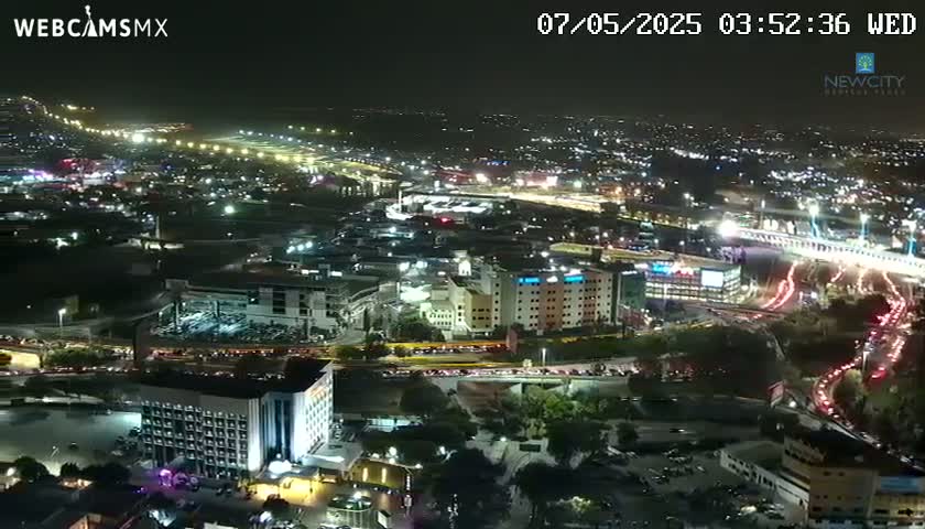 A nighttime aerial view shows a sprawling city with brightly lit roads and buildings, under a clear sky.