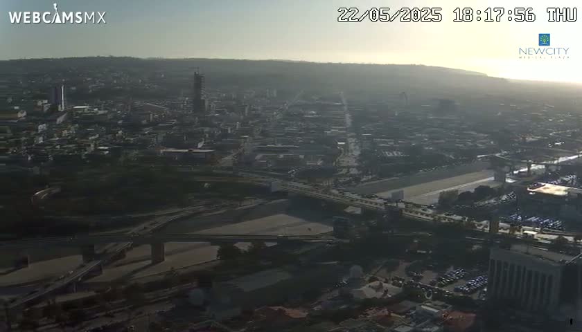 A hazy sunset illuminates a sprawling city with bridges and roadways visible from a high vantage point.