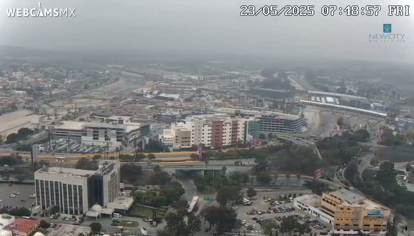 A hazy, high-angle view shows a sprawling urban landscape with numerous buildings, roads, and a large parking lot, possibly near a racetrack.
