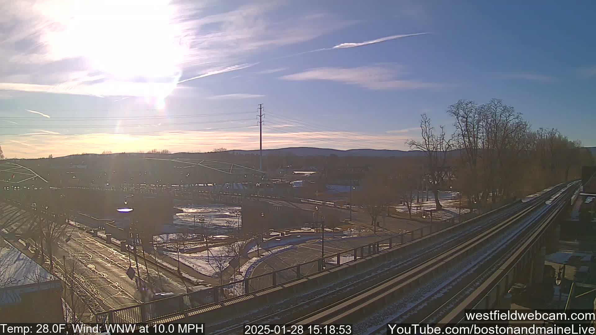 A partly sunny day with a WNW wind at 10 mph shows a view of a town with train tracks and some snow on the ground.