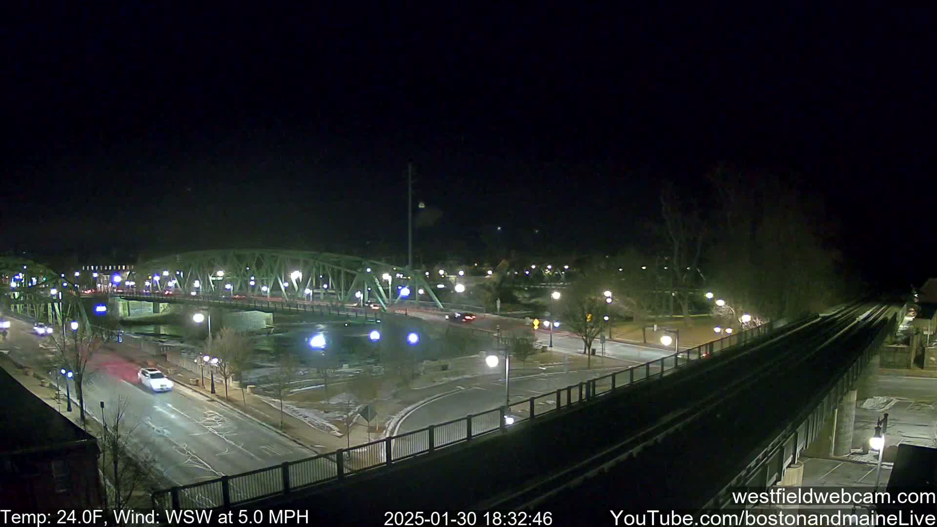 A nighttime view of a bridge over a river with sparse traffic, under a clear, dark sky and a temperature of 24 degrees Fahrenheit, with a wind blowing from the west-southwest at 5 mph.