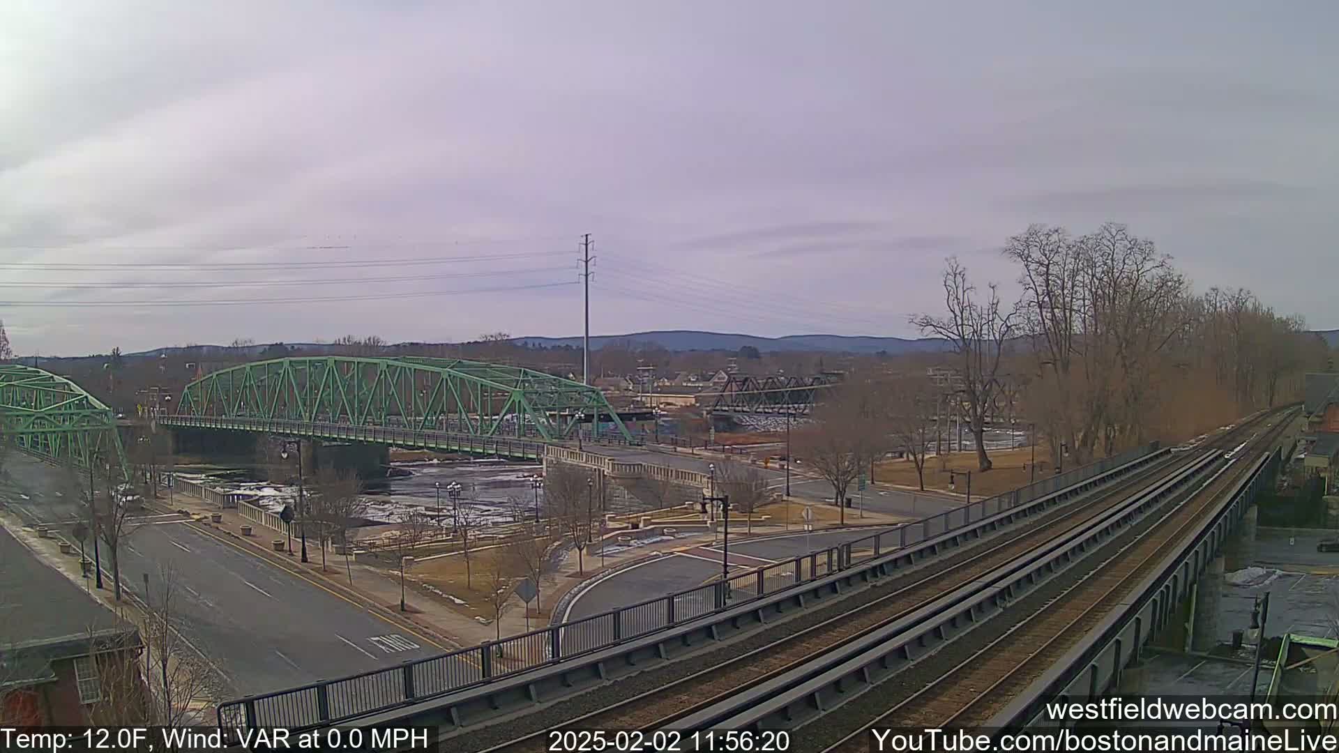 A view of two bridges over a river, with train tracks and a road leading to them, under a cloudy sky.