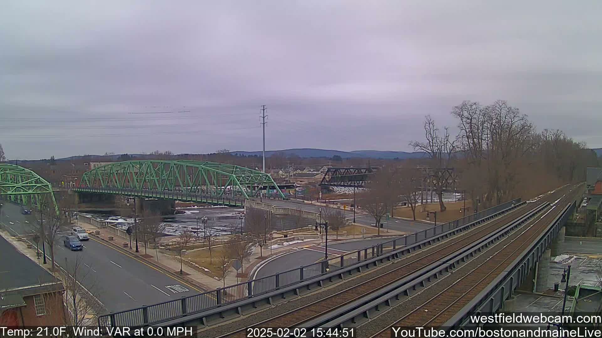 A view of a town with two bridges over a partially frozen river, under an overcast sky.
