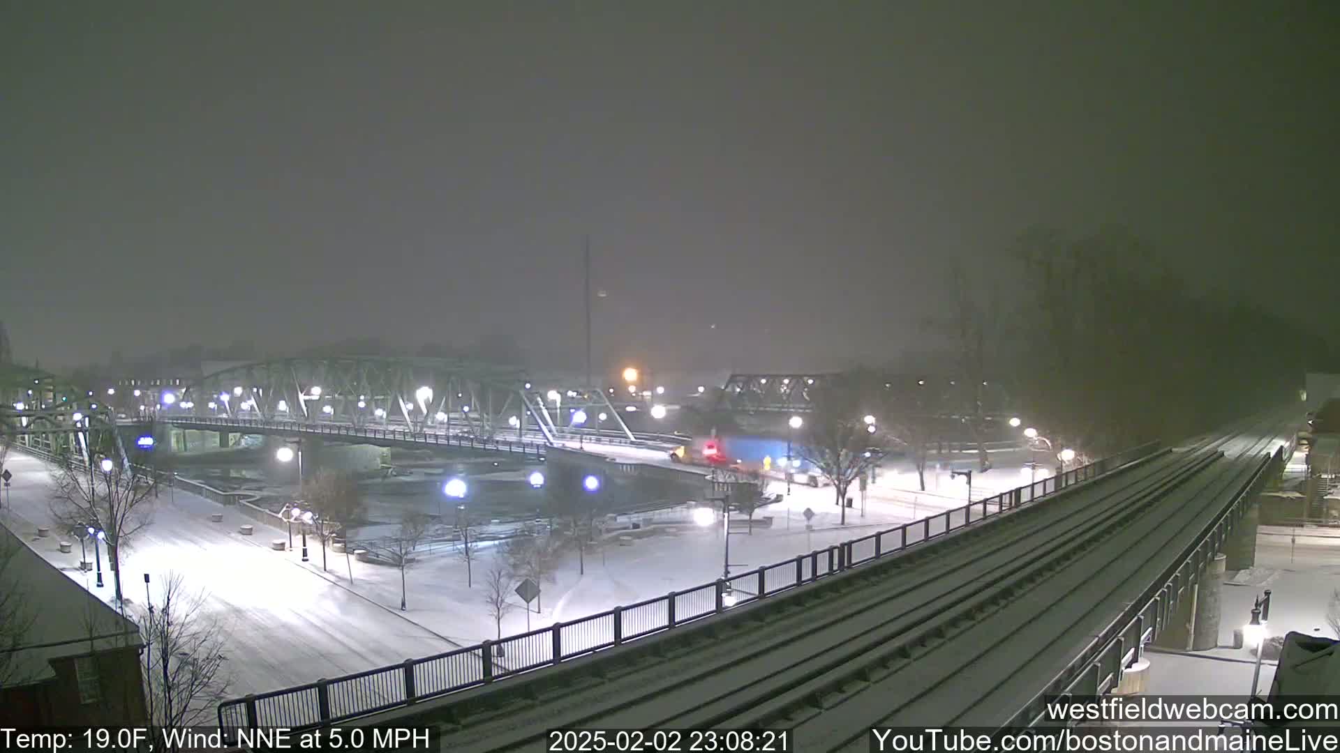 A snow-covered bridge and train tracks are visible under a heavy snowfall at night.