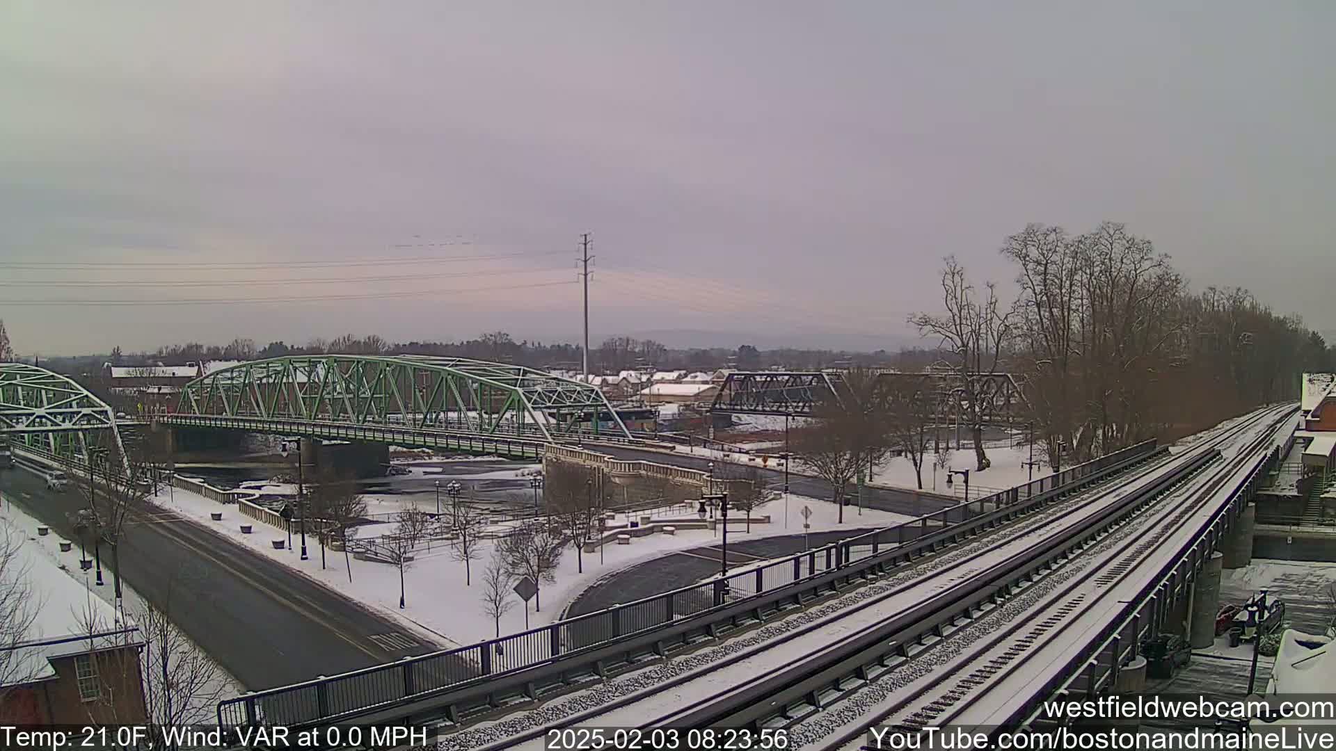A snow-covered landscape with two bridges and train tracks, under a cloudy sky.