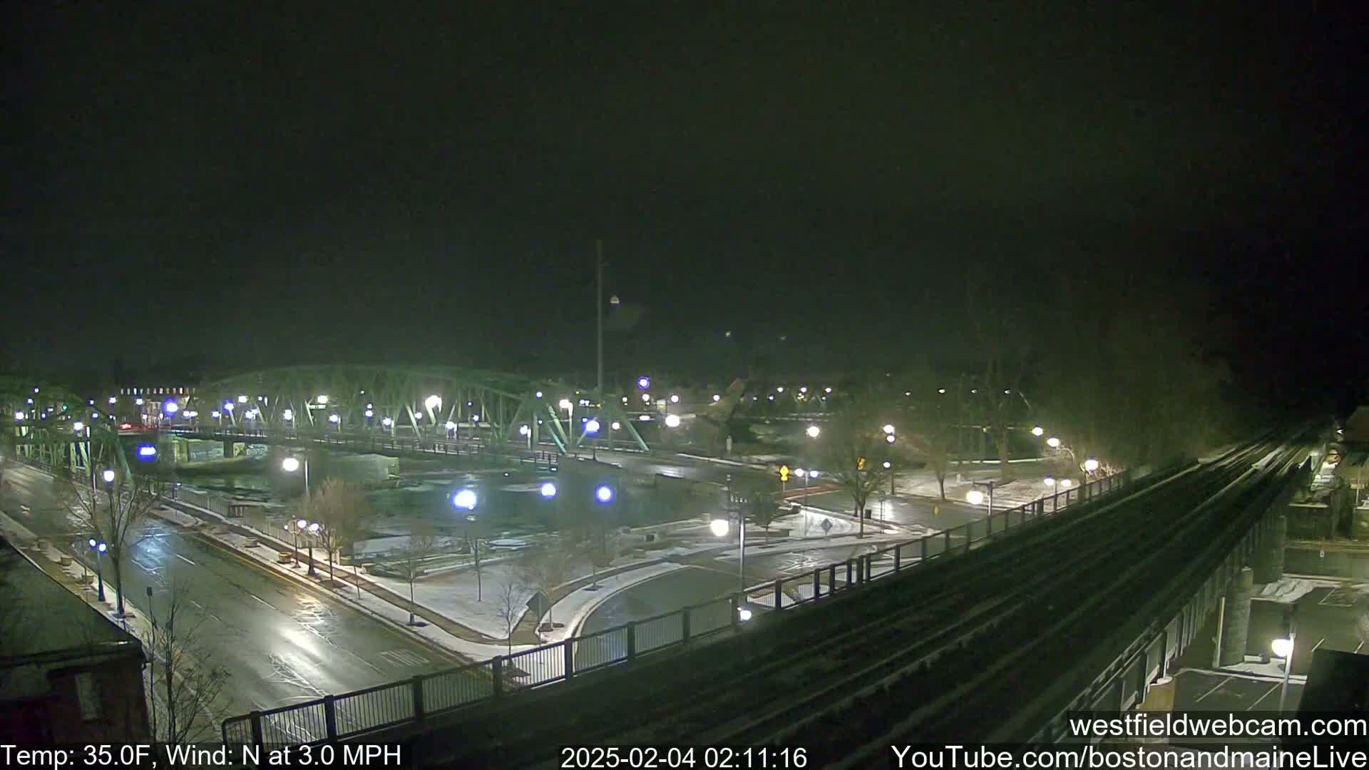 A nighttime view of a bridge and roadways with light snow on the ground and a temperature of 35 degrees Fahrenheit, with a 3 mph northerly wind.