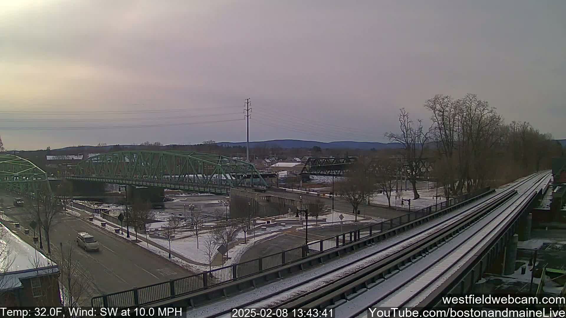 A view of a town with two bridges over a river, partially covered in snow, under an overcast sky.