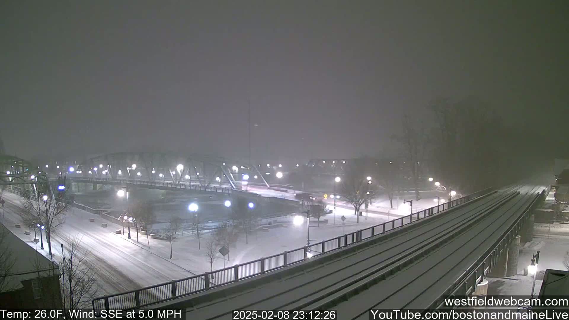 A snow-covered bridge and city street are seen under a hazy, snowy night.