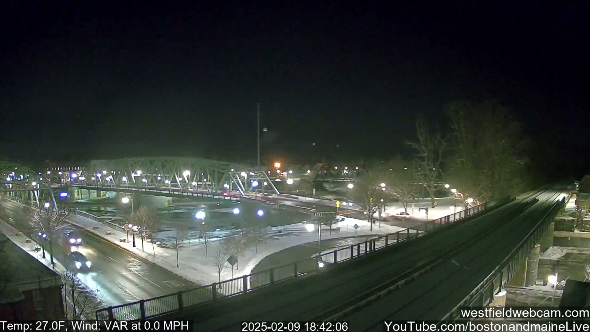 A snow-covered bridge and roadway are illuminated at night, with a few vehicles visible.