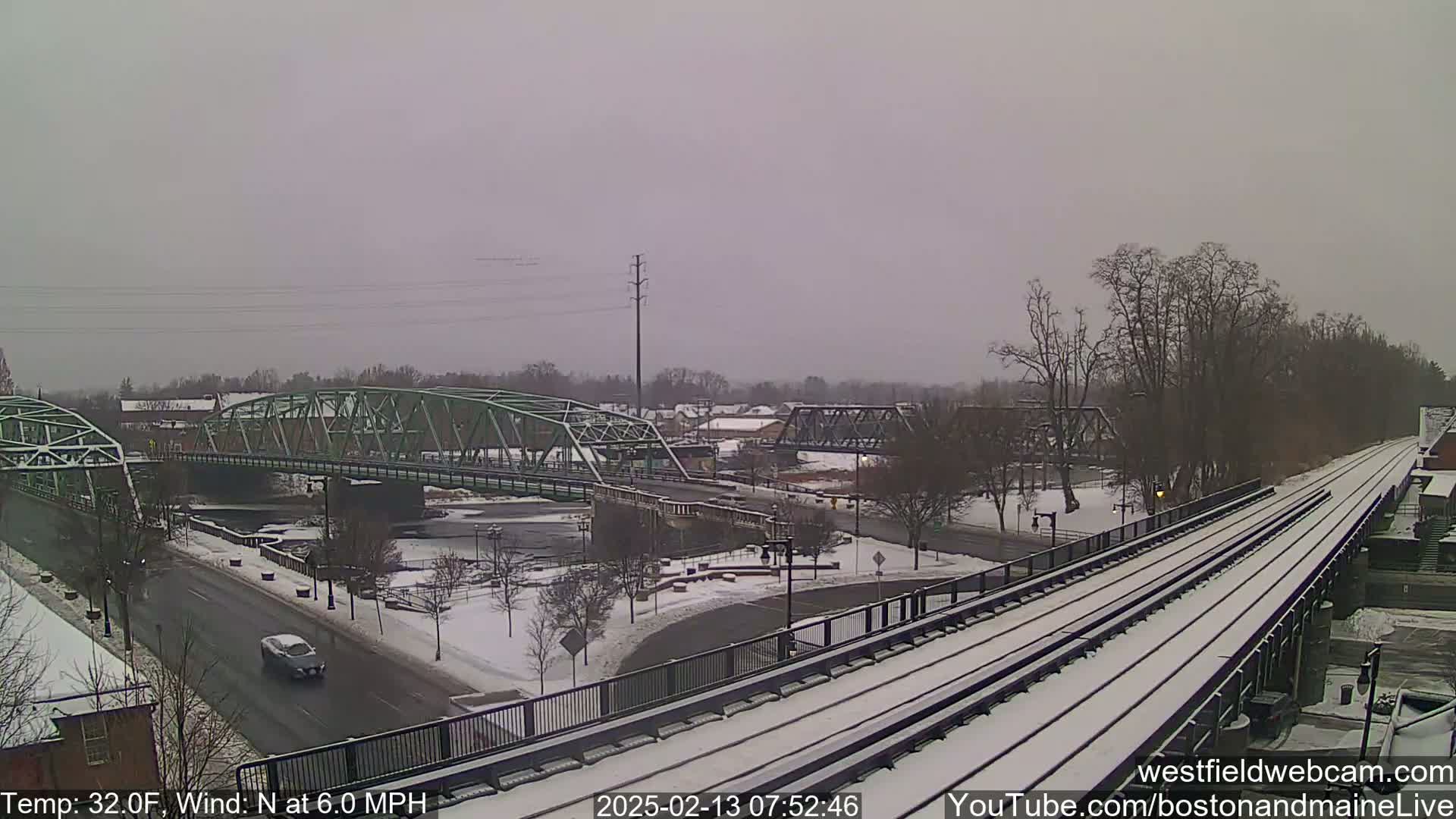 A snow-covered train track and two bridges over a river are seen in a light snowfall.