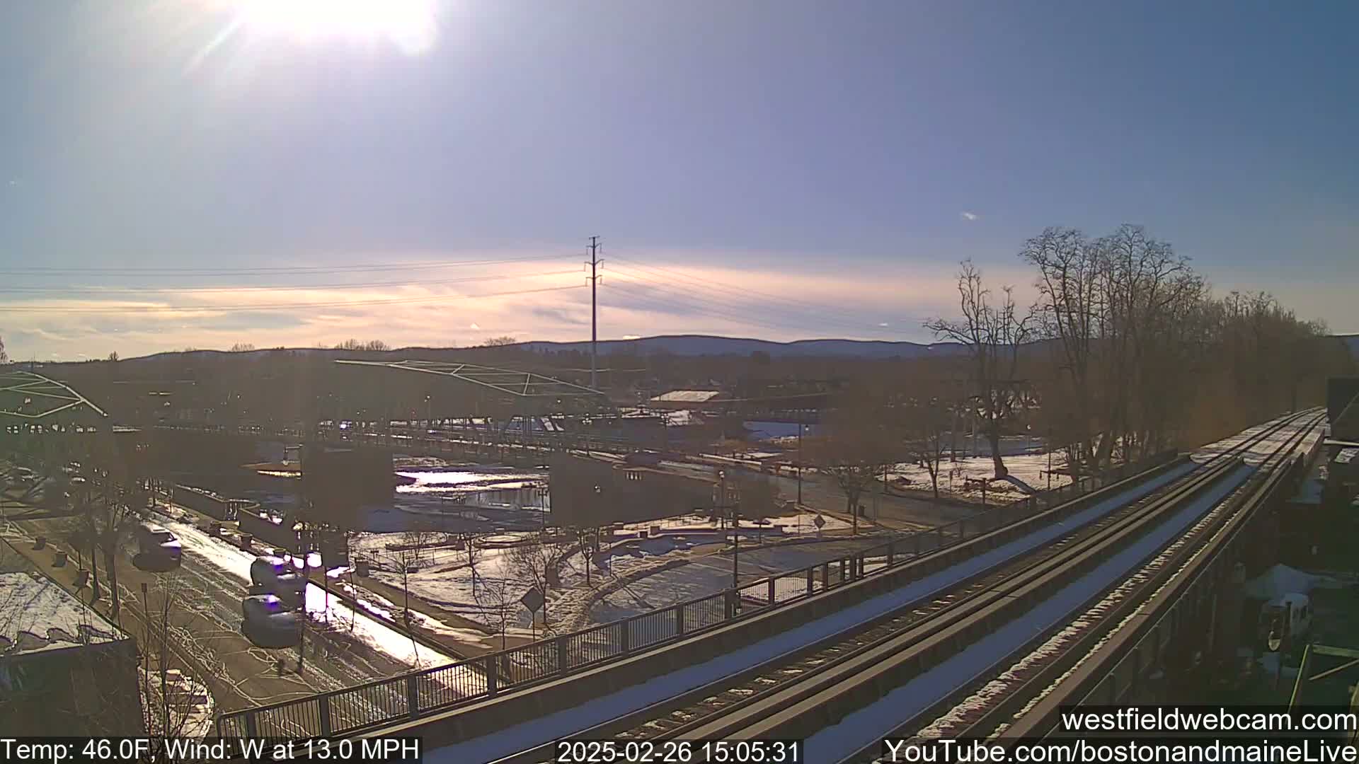 A sunny, slightly windy day overlooks a snow-dusted town with train tracks in the foreground and a river running through it.