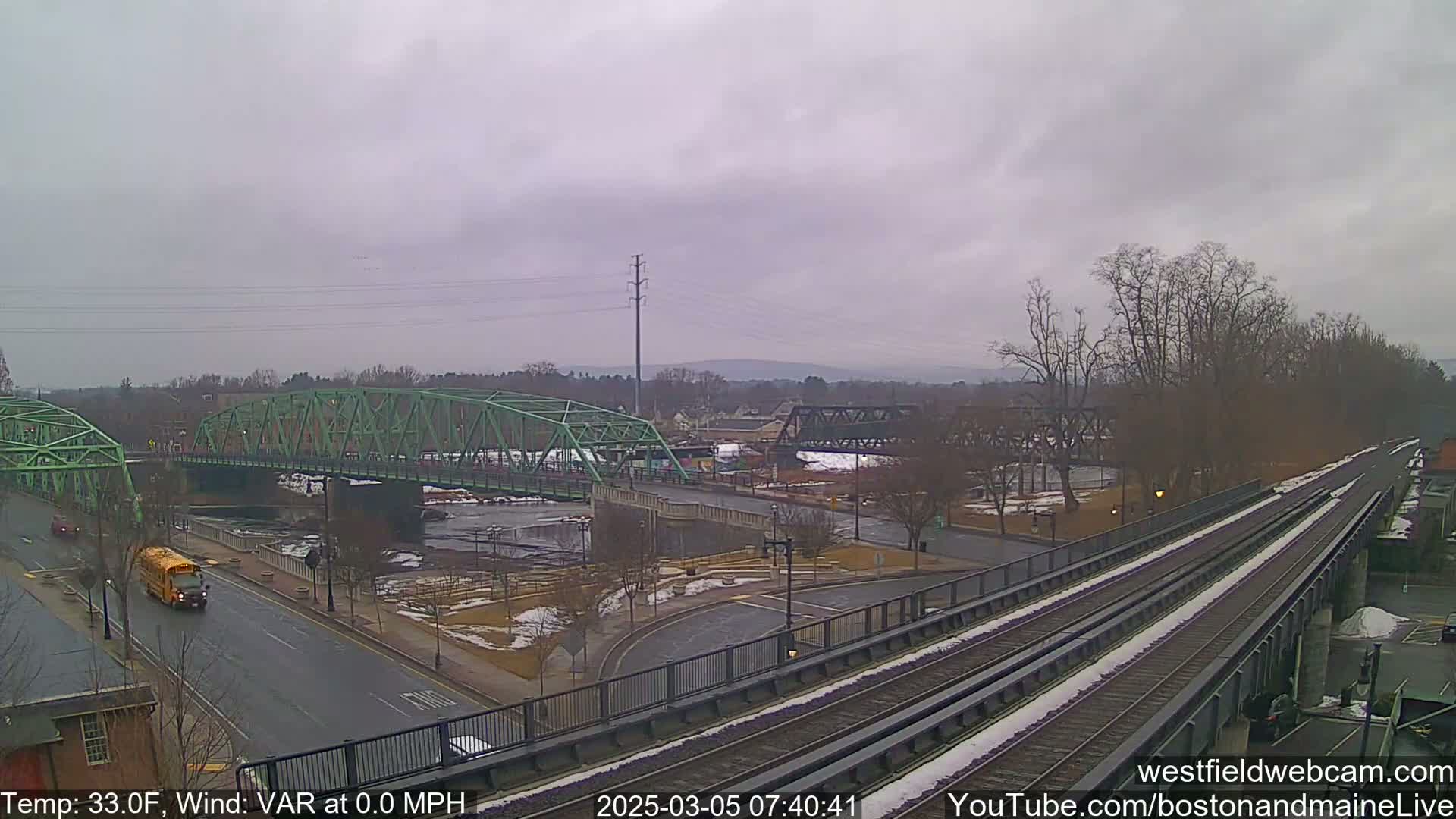 A view of two bridges over a river, a train track, and a roadway, under an overcast sky.