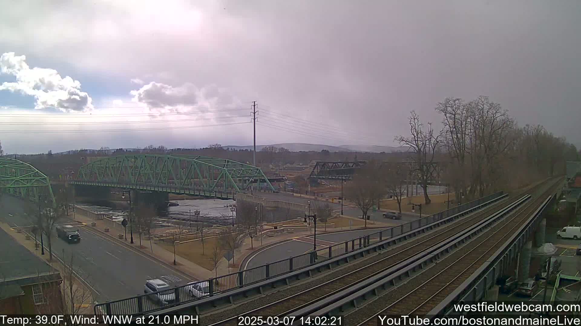 A view of a town with two bridges over a river, under an overcast sky with a strong wind.