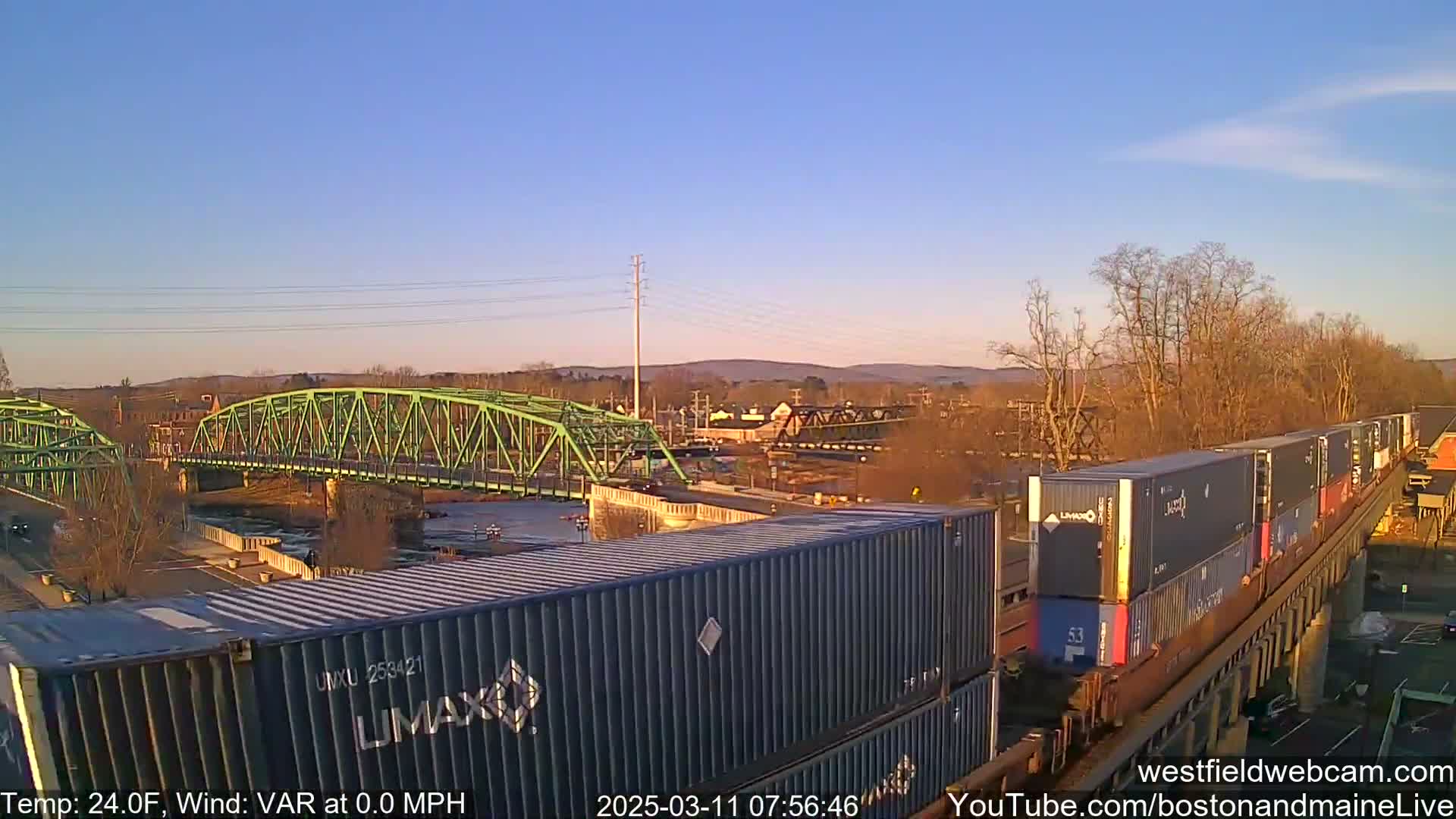 A freight train carrying shipping containers travels across a bridge on a clear, cold day.