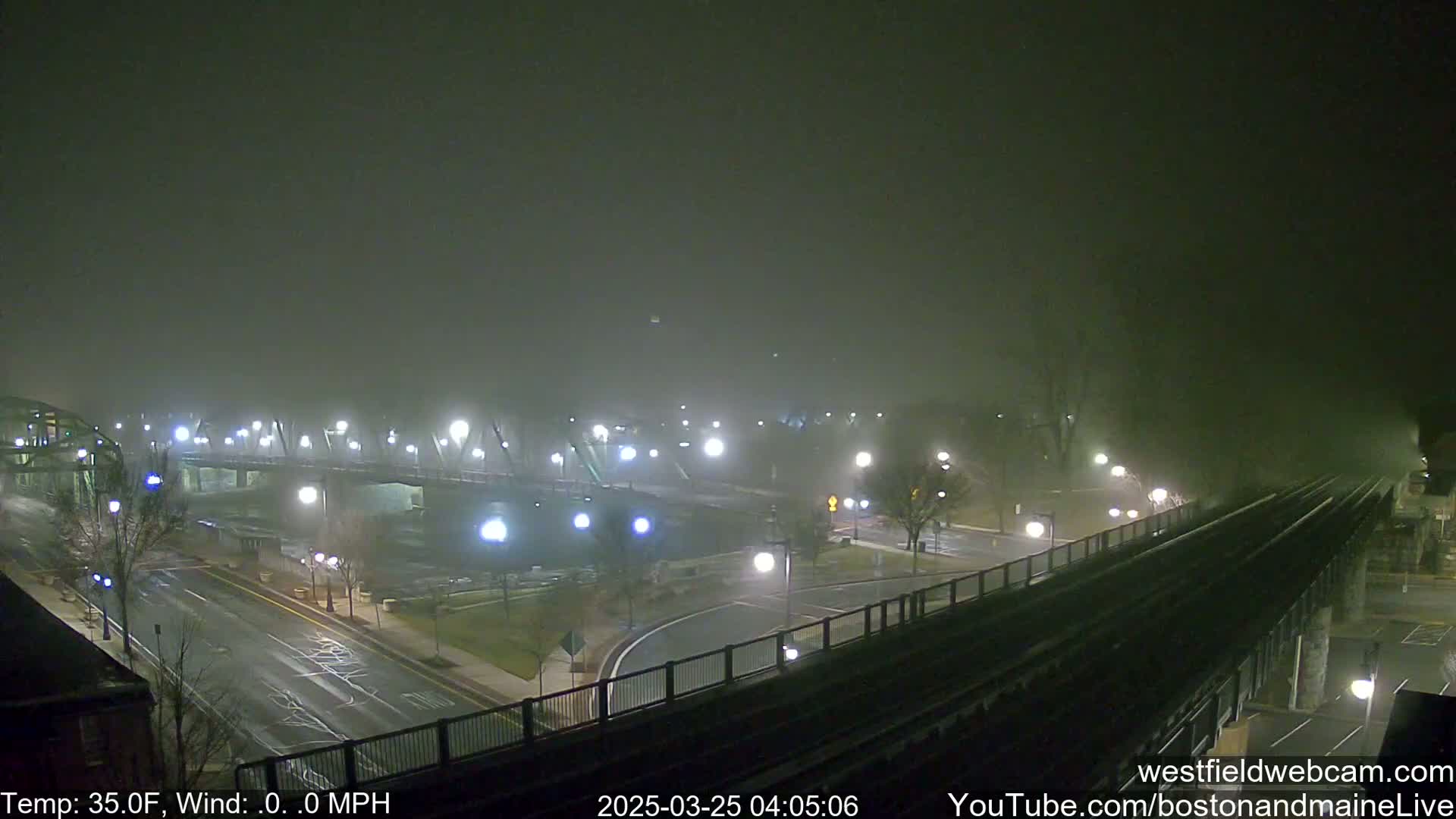 A bridge and roads are dimly lit under a thick fog at night.