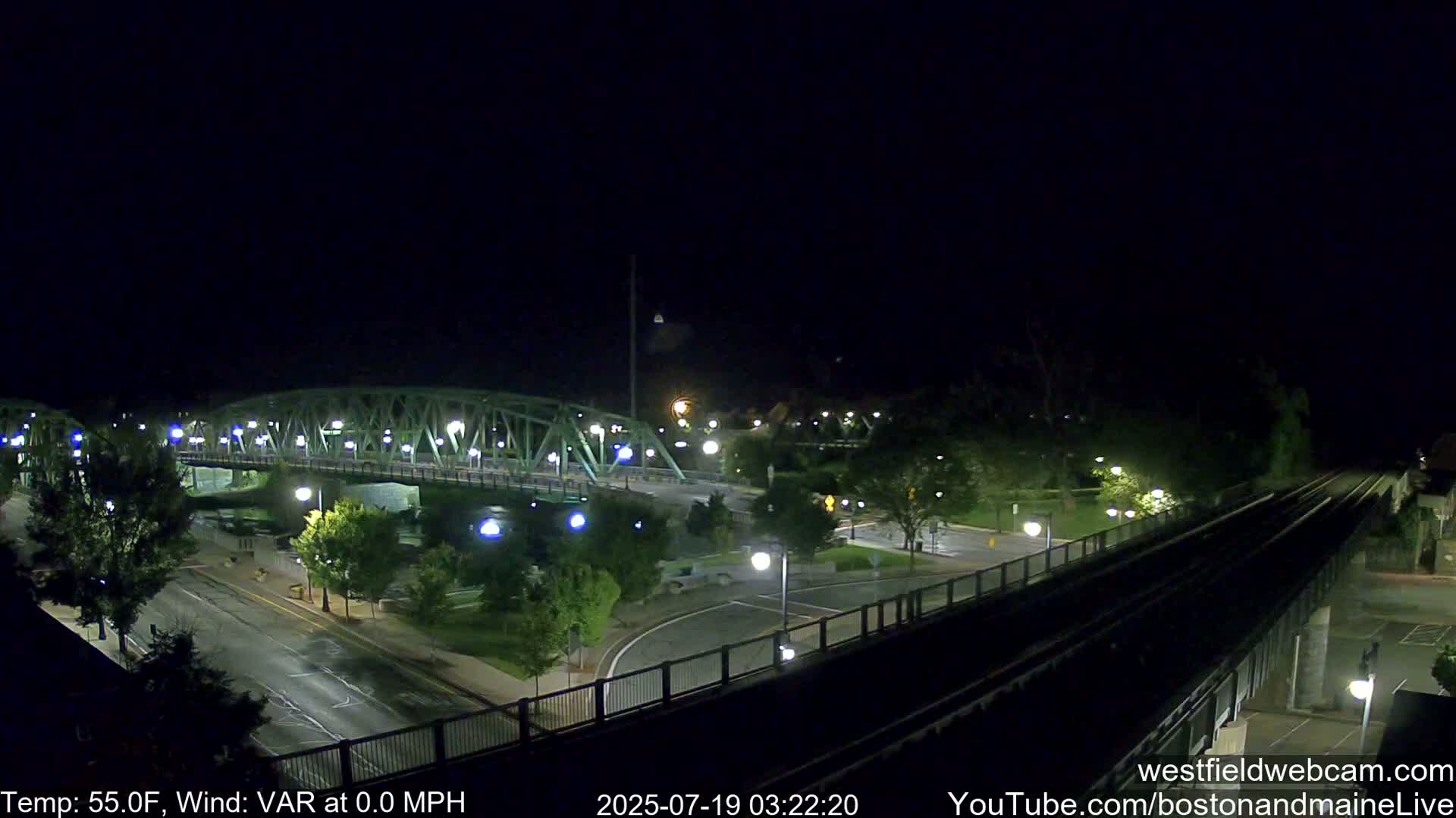 A nighttime view of a bridge and roadway intersection, with calm weather conditions.