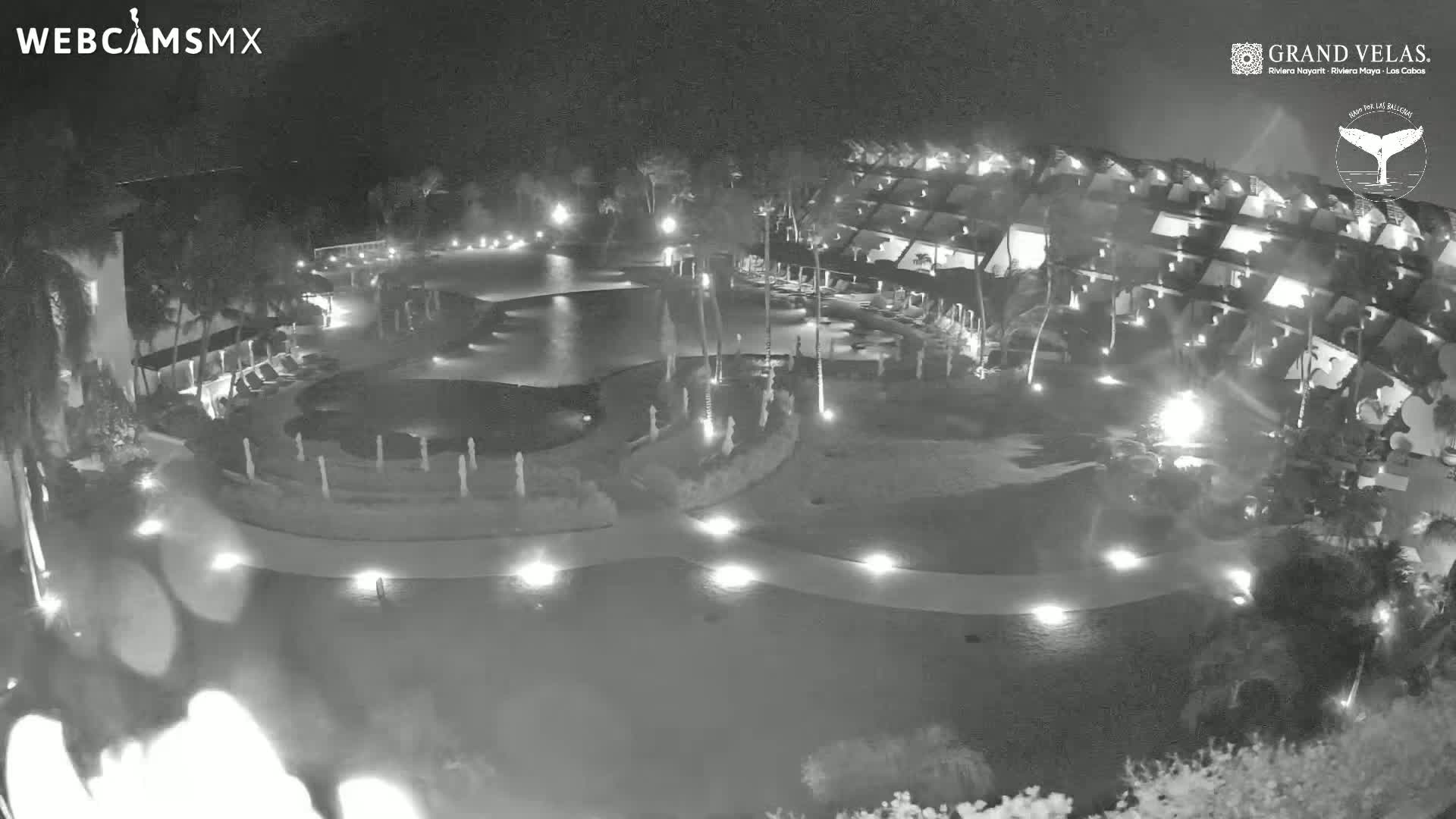 A nighttime aerial view of a resort with a pool and surrounding buildings illuminated by lights.