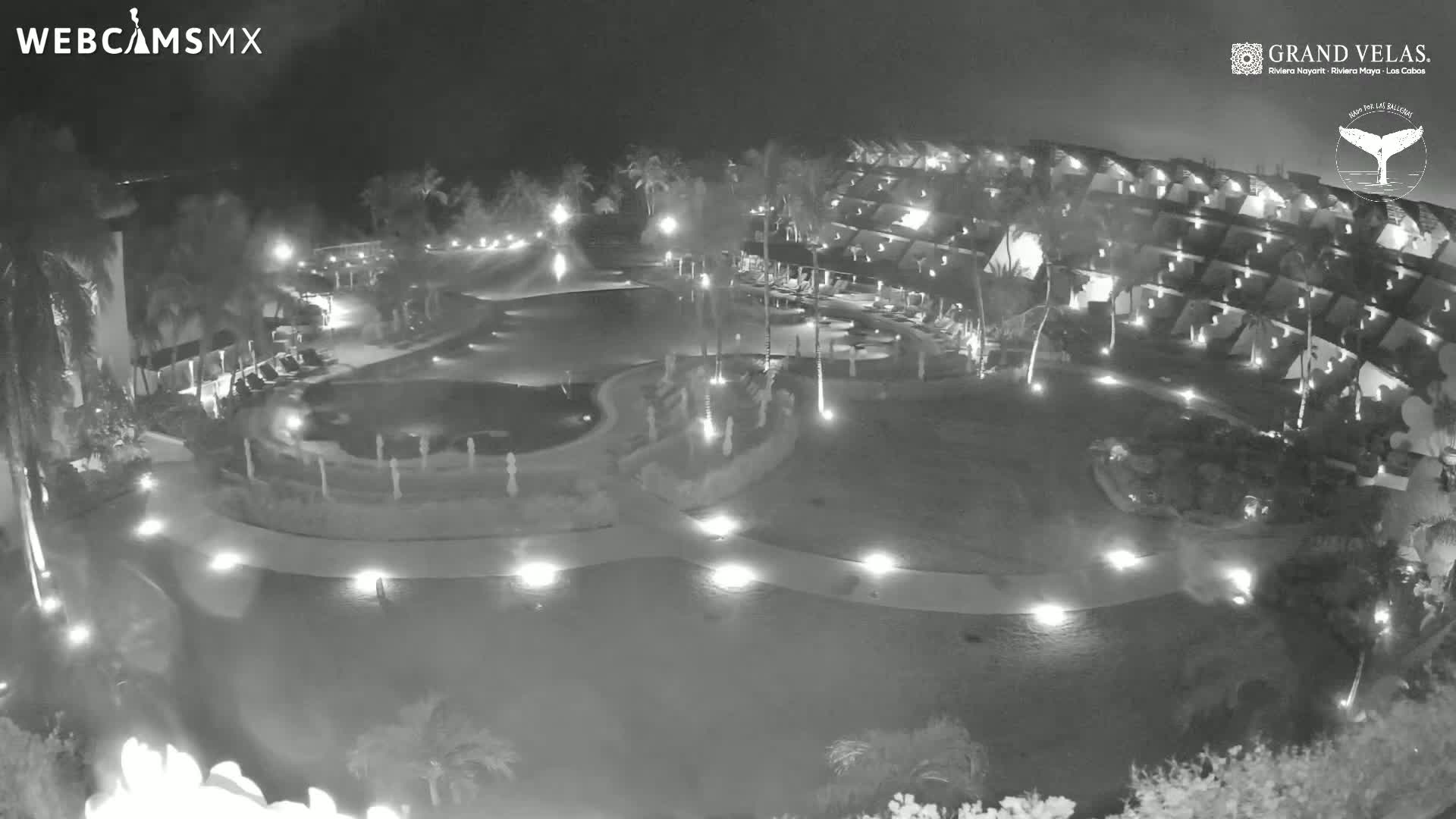 A nighttime aerial view of a resort complex with pools and buildings illuminated by lights.