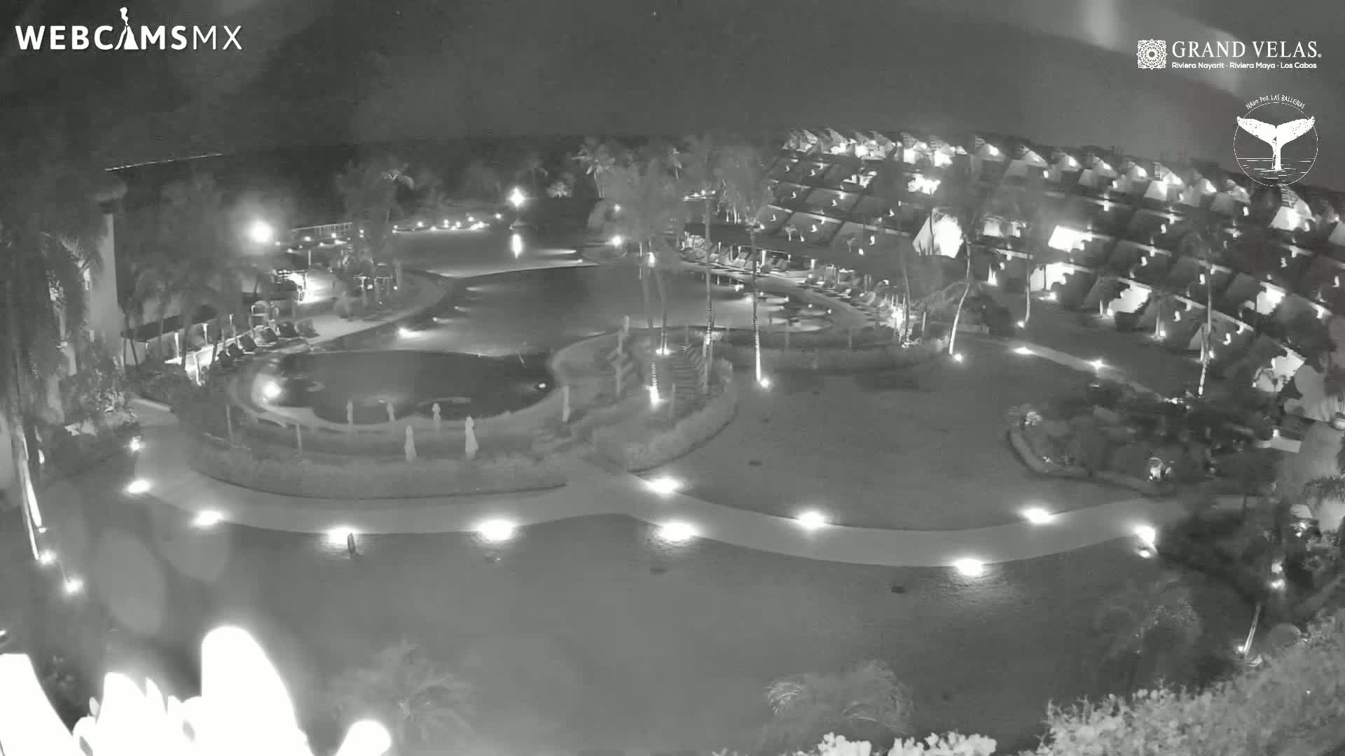 A nighttime, high-angle view of a resort complex with a swimming pool and walkways illuminated by lights.
