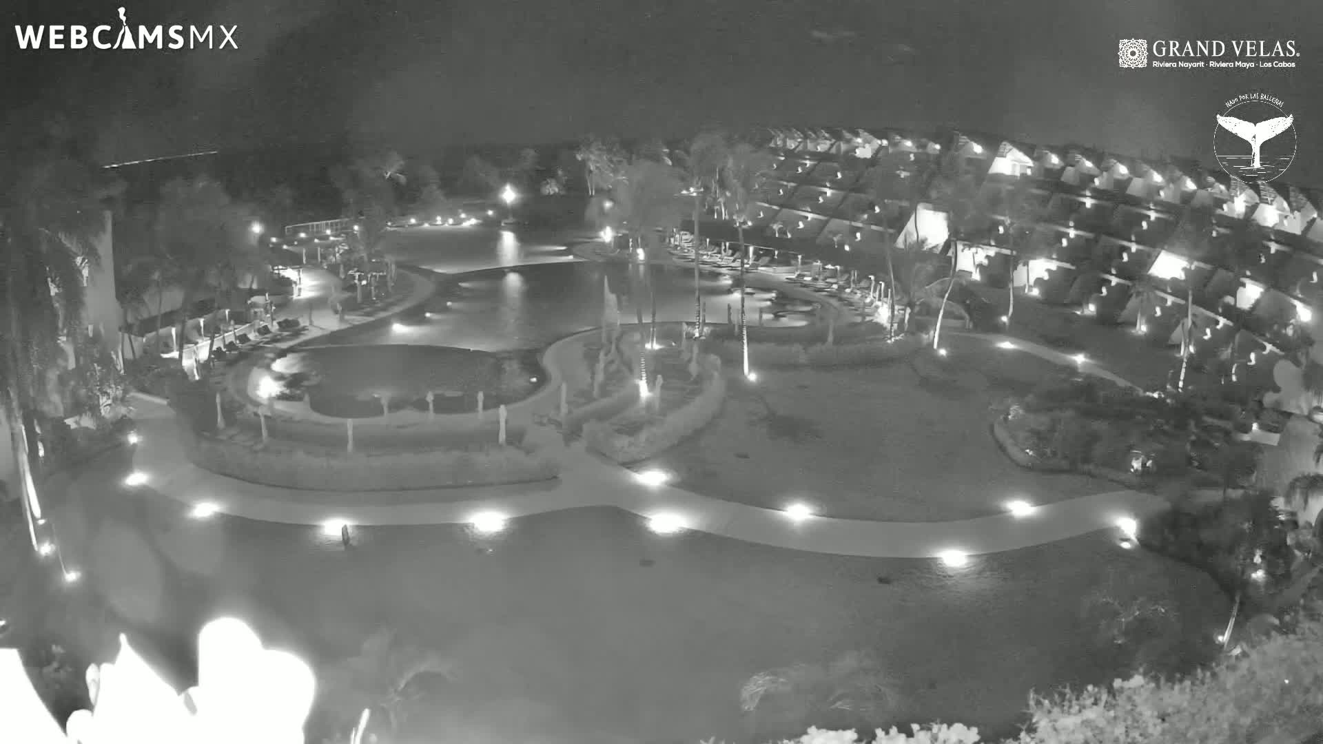 A nighttime, high-angle view of a resort's pool and surrounding buildings, lit by outdoor lights.