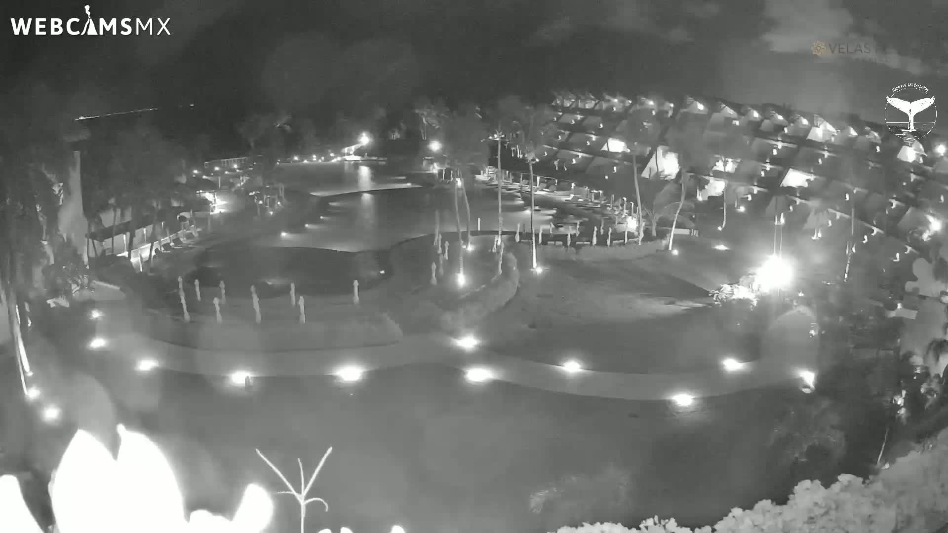 A nighttime, black-and-white view of a resort complex with a pool and surrounding buildings illuminated by lights.